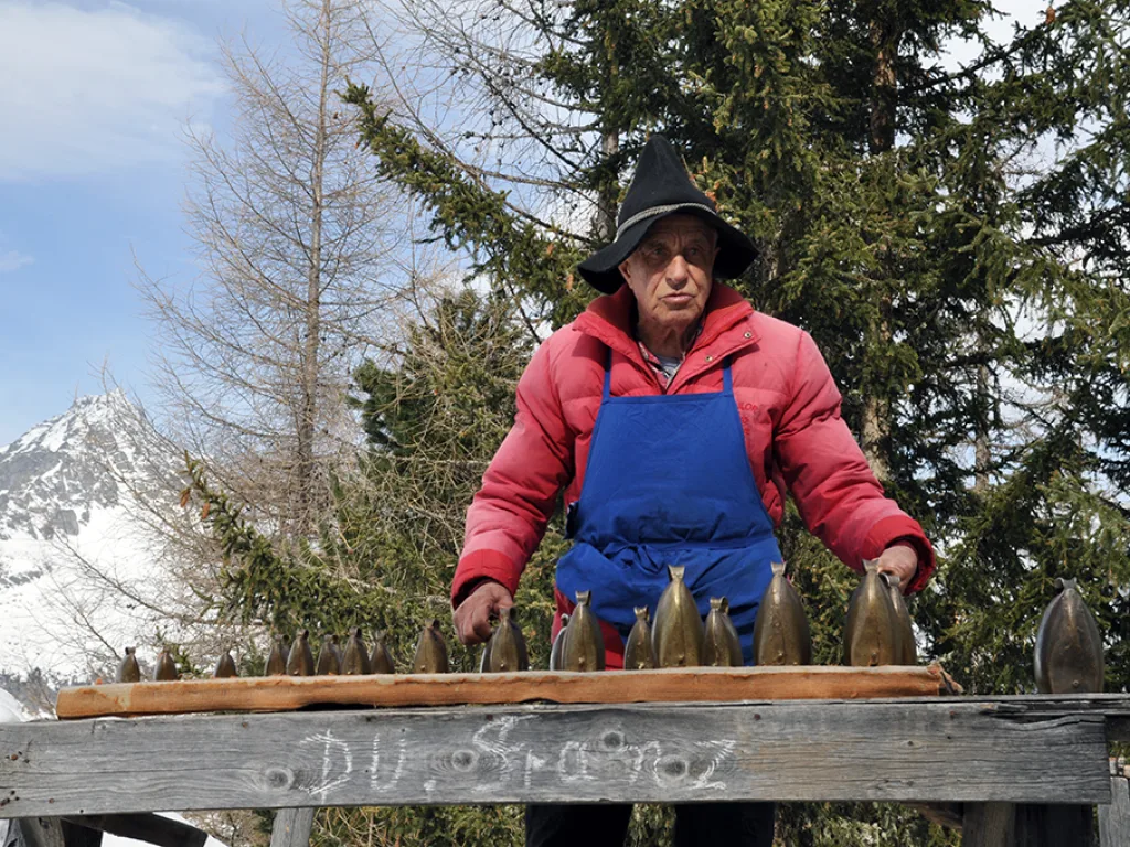 Person in blauer Schürze steht an der Glockenreihe vor der Hütte.